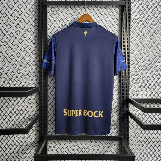 Maillot de football bleu marine avec manches imprimées et logo Super Bock suspendu sur grille métallique