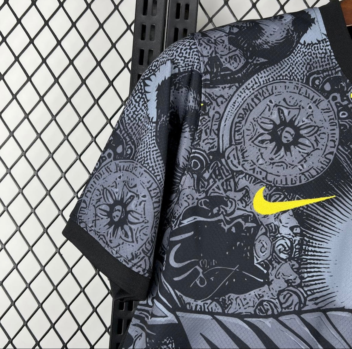 T-shirt Nike noir et gris avec motifs circulaires et logo swoosh jaune accroché à une grille noire