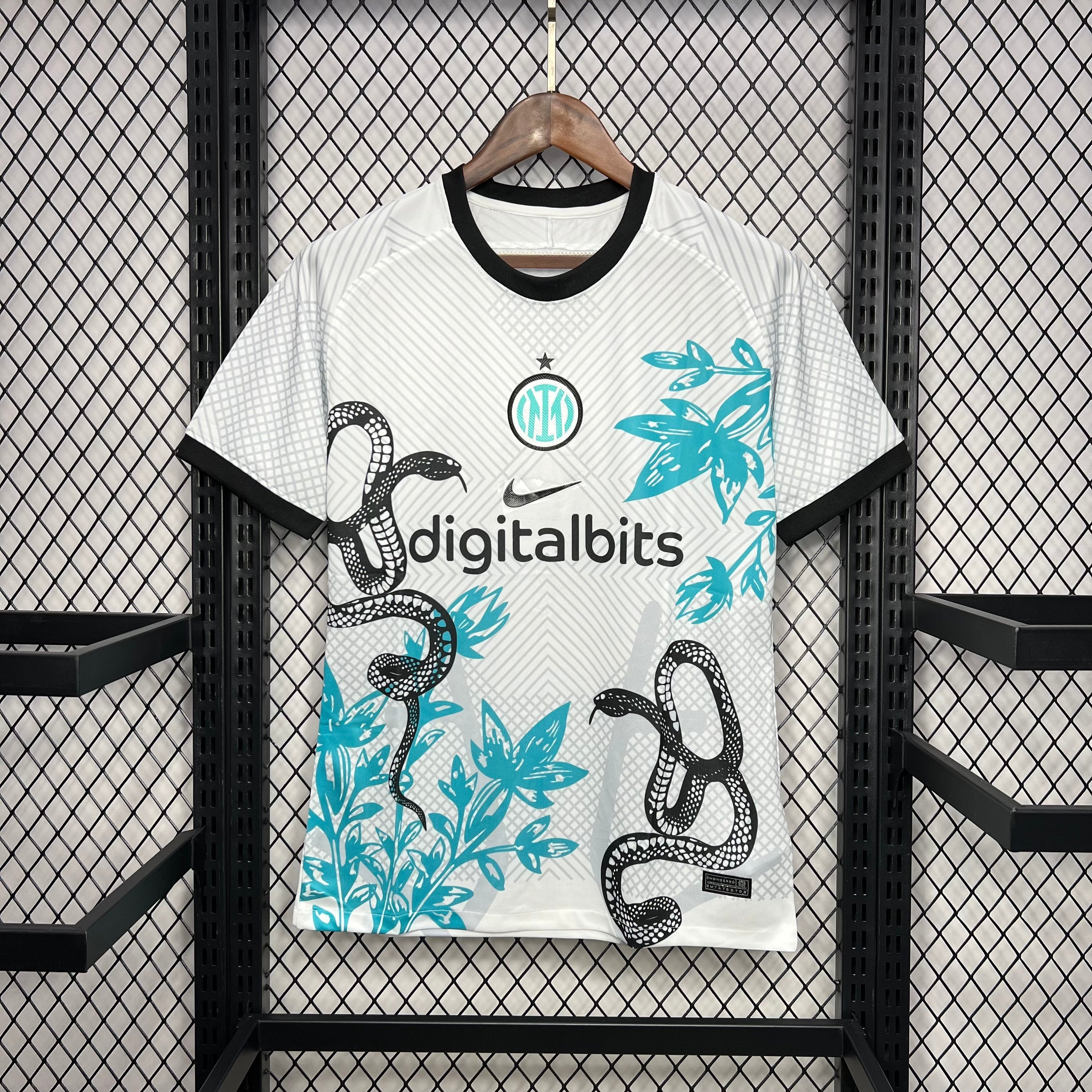 Maillot de football Inter Milan 2024 blanc avec motifs serpent noir et feuillage bleu accroché sur fond grillagé