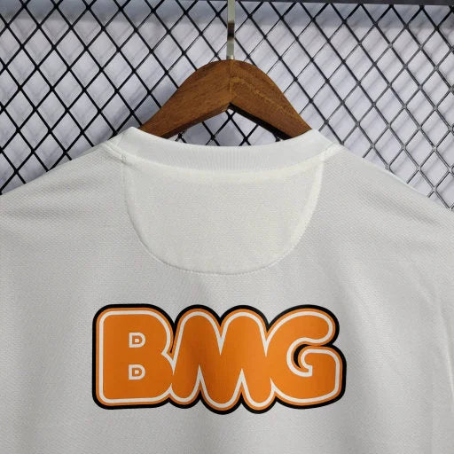 Détail du haut d'un maillot blanc avec logo BMG orange sur un cintre en bois et fond grillagé